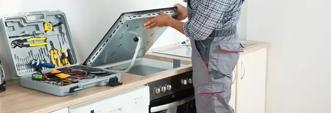 Cooktop repair technician lifting a built-in stovetop for service in Spokane, WA