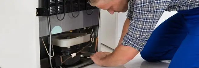 Refrigerator repair technician servicing the compressor and condenser area in Spokane, WA