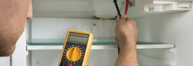 Refrigerator repair technician testing electrical components with a multimeter in Spokane, WA