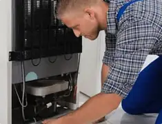 Refrigerator repair technician servicing the compressor and condenser area in Spokane, WA